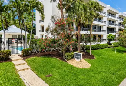 The Corniche Oceanfront Condominium in Boca Raton featuring white exterior balconies, lush landscaping, palm trees, and private pool entrance.