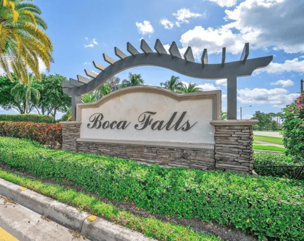 Entrance sign for Boca Falls in Boca Raton, surrounded by greenery against the blue skies.