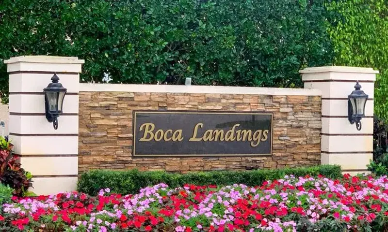Entrance sign for Boca Landings in Boca Raton, surrounded by flowers, greenery, and tropical landscaping.