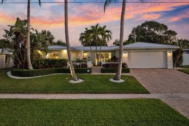 Front view of a single-story home in Chatham Hills Boca Raton with tropical landscaping, palm trees, and a sunset sky.