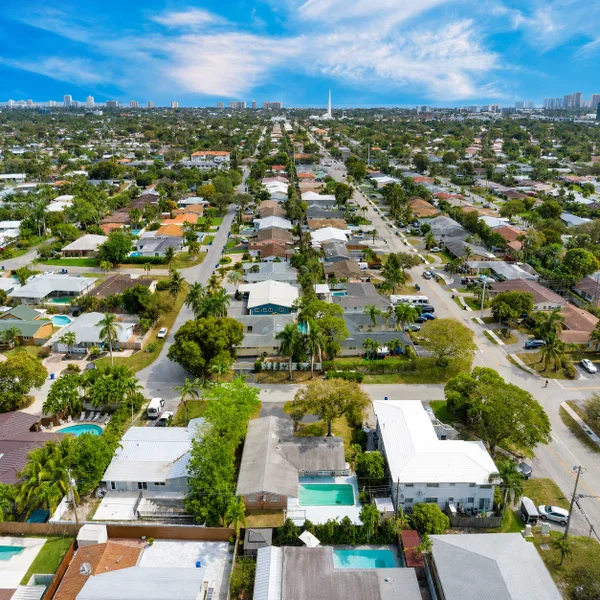 Aerial view of Coral Ridge Isles in Fort Lauderdale, FL with homes, palm-lined streets, pools, and South Florida skyline.