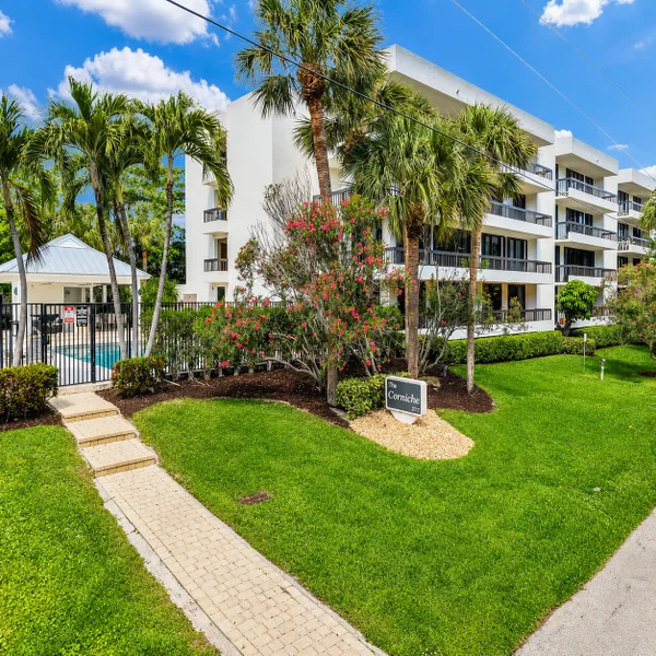 The Corniche Oceanfront Condominium in Boca Raton featuring white exterior balconies, lush landscaping, palm trees, and private pool entrance.