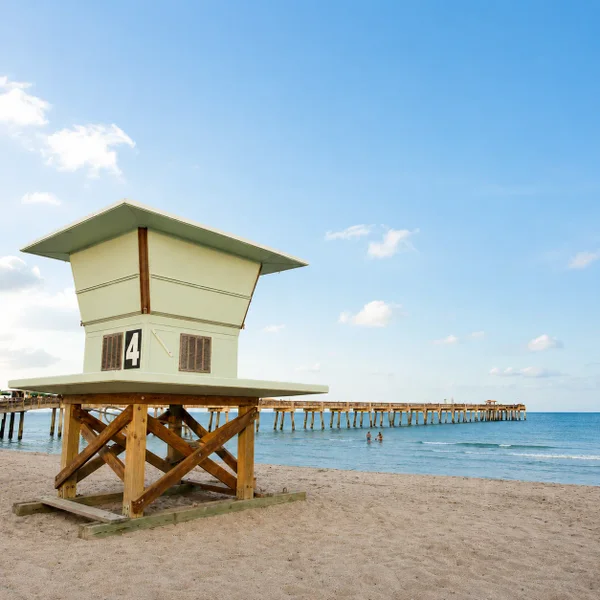 Sunny Dania Beach oceanfront scene with lifeguard tower, sandy beach, and pier in South Florida near waterfront homes.