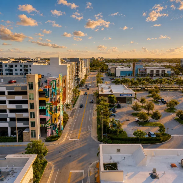 Dania Beach City South FL luxury real estate view with modern apartments, retail plazas, palms, and golden-hour city streets.