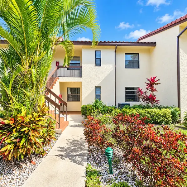 Glades of Boca Lago Boca Raton 55+ condo building with palm trees, garden walkway, and sunny South Florida setting.