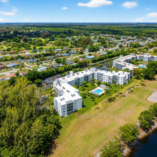 Greenacres luxury real estate aerial in South Florida with condo buildings, pool amenities, green space, and nearby golf course views.