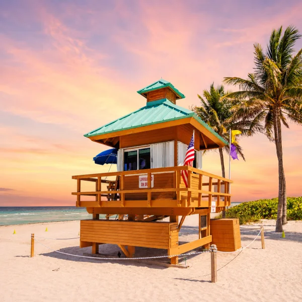 Sunny Isles Beach lifeguard tower at sunset with palm trees, ocean views, sandy beach, and South Florida coastal scenery.