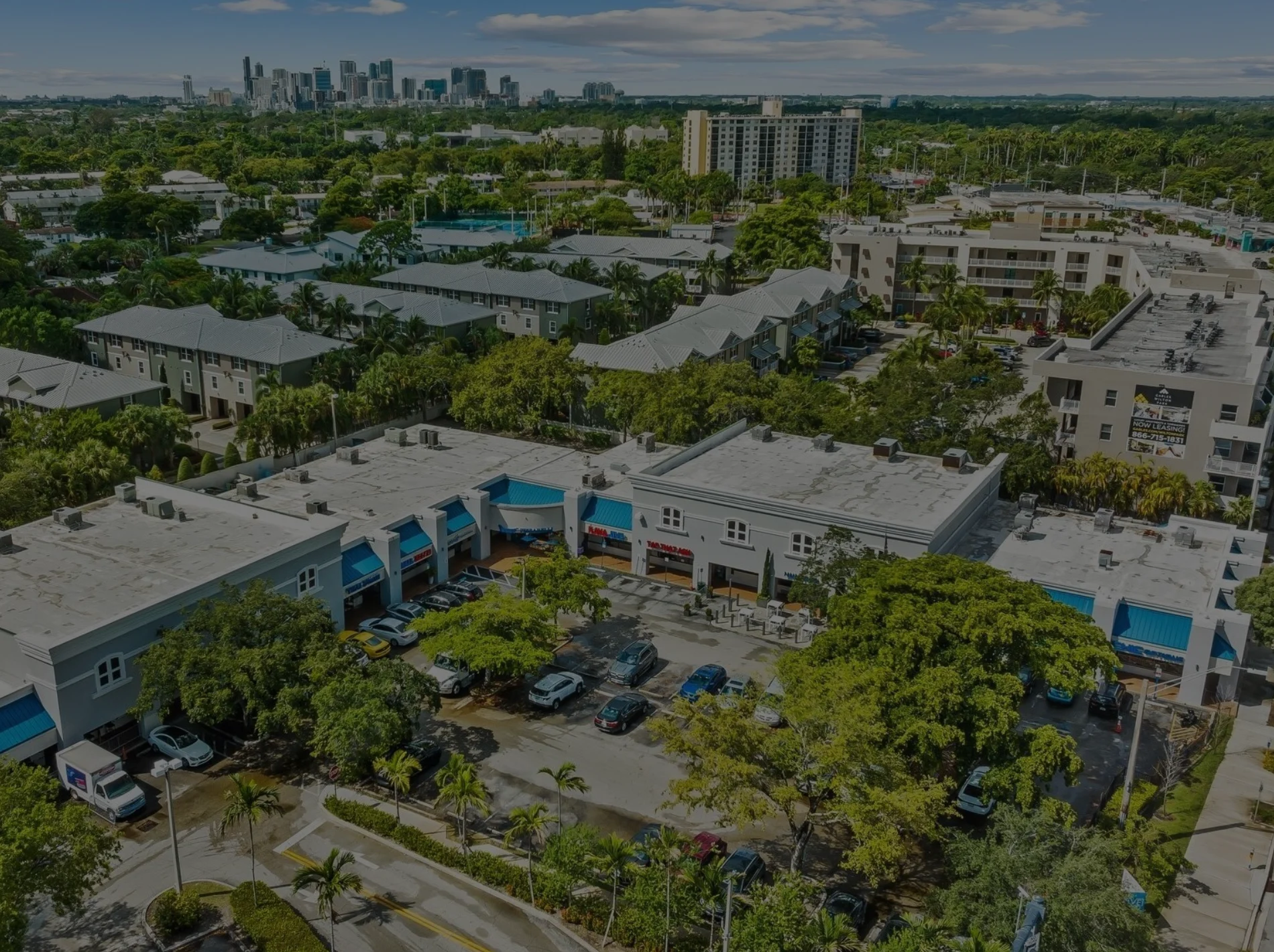 Aerial view of Wilton Manors with palm trees and high-rise buildings under a bright blue sky.