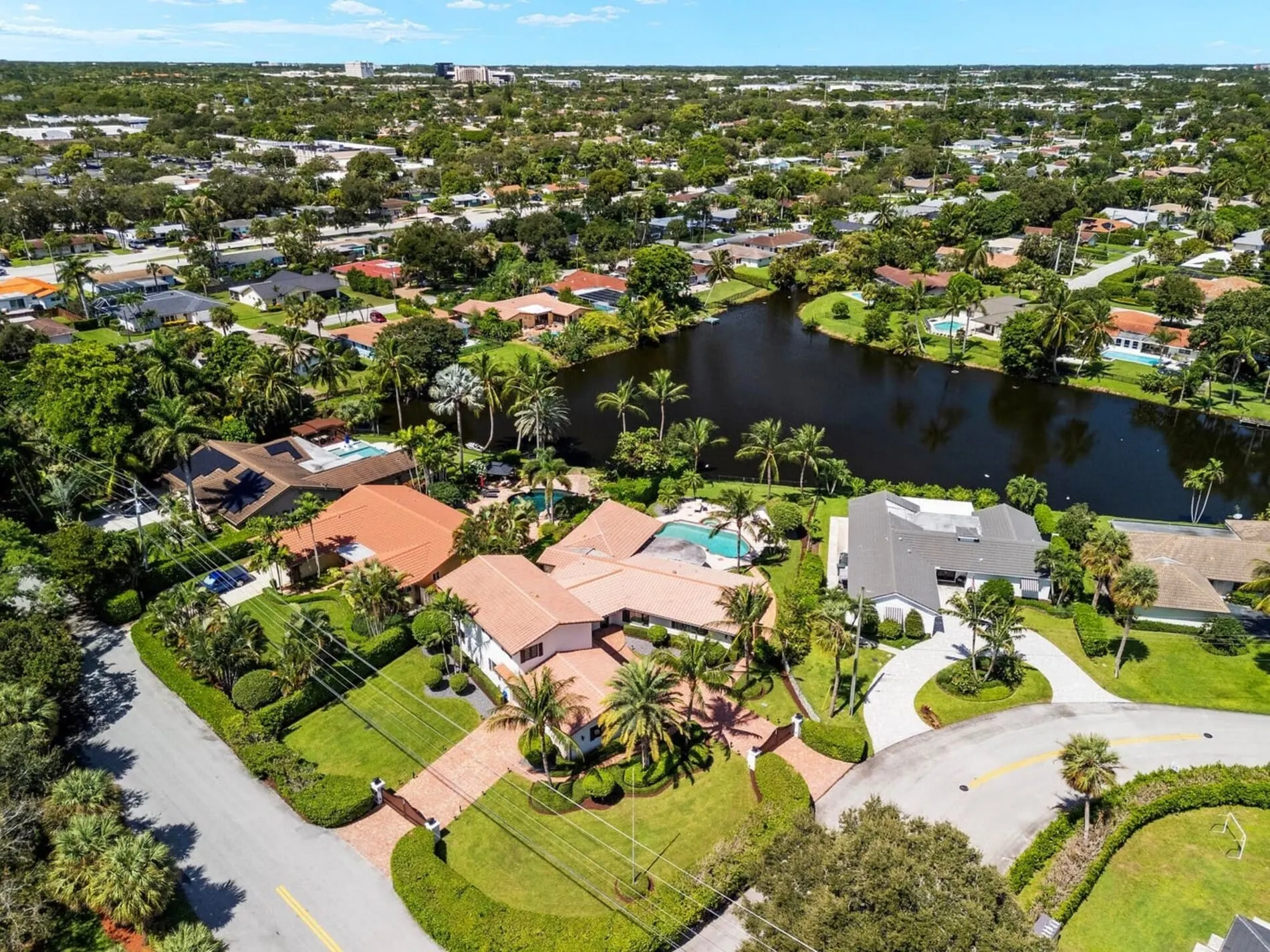 Aerial view of Lake Floresta Park neighborhood with waterfront homes, pools, tropical landscaping, and a winding lake.