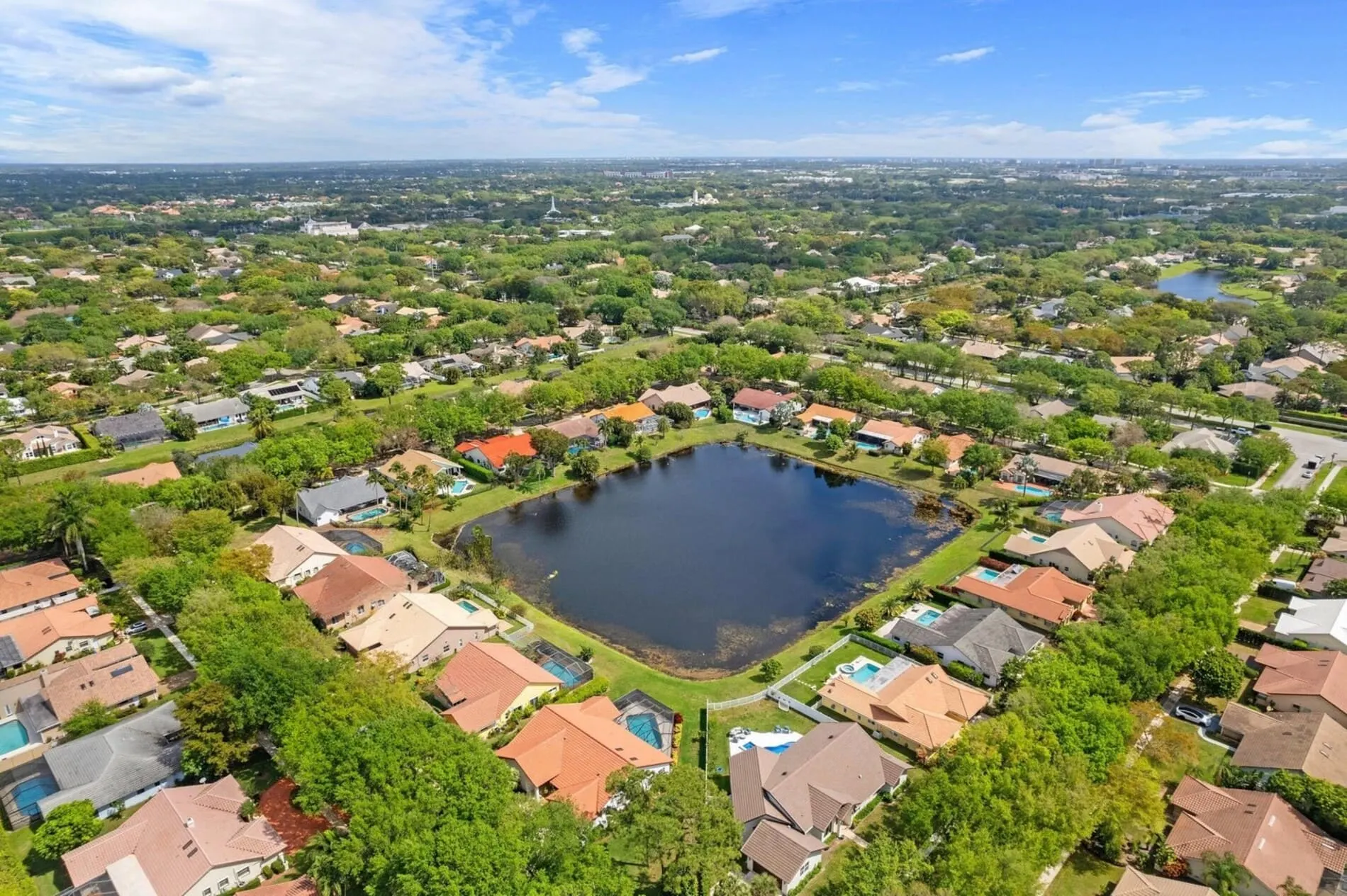 Aerial view of Lakewood Oaks community featuring homes with pools surrounding a central lake and tree-lined streets.
